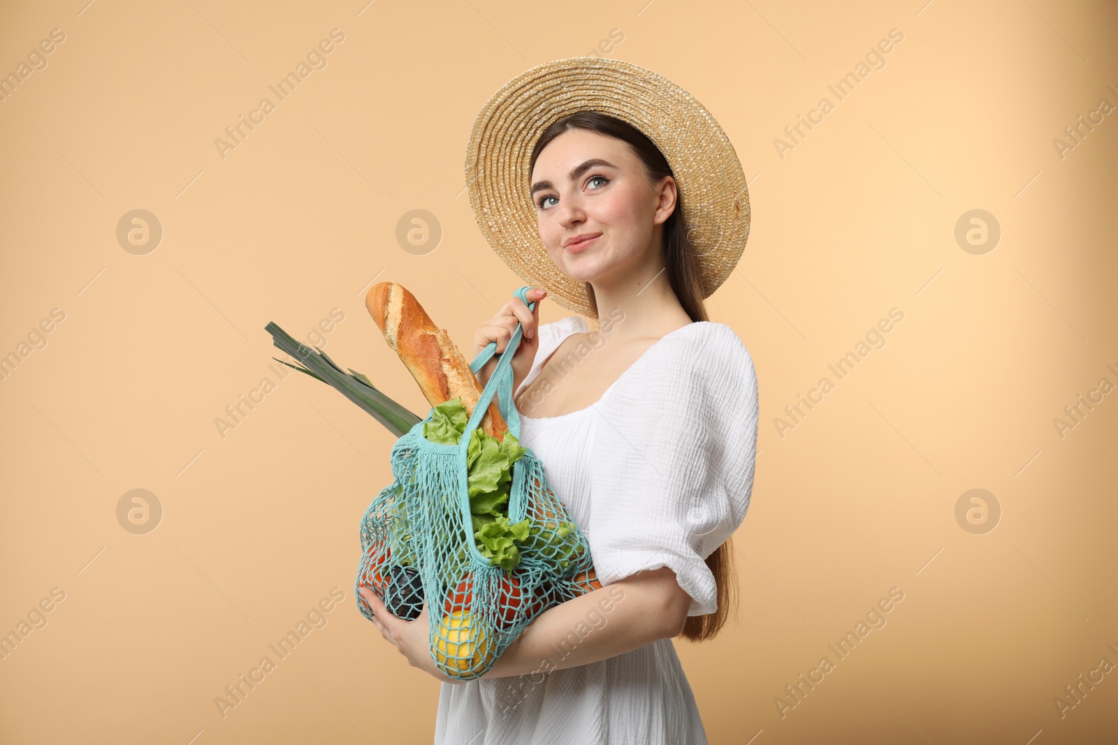 Photo of Woman with string bag of fresh vegetables and baguette on beige background