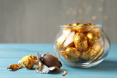 Chocolate eggs wrapped in golden foil on light blue wooden table. Space for text