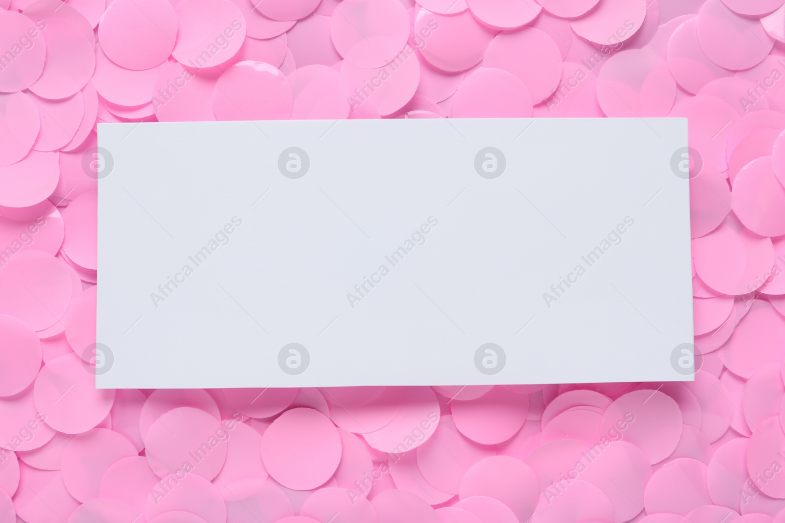 Photo of Blank white card on pink confetti, top view. Space for text