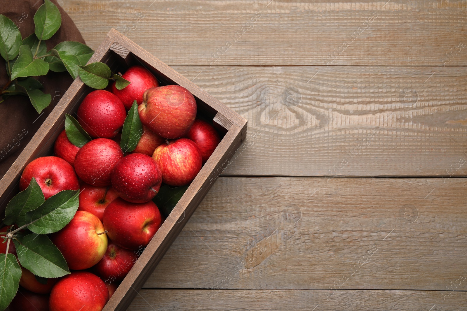 Photo of Crate with wet red apples and green leaves on wooden table, flat lay. Space for text