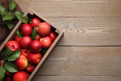 Photo of Crate with wet red apples and green leaves on wooden table, flat lay. Space for text