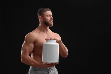 Young man with muscular body holding jar of protein powder on black background, space for text