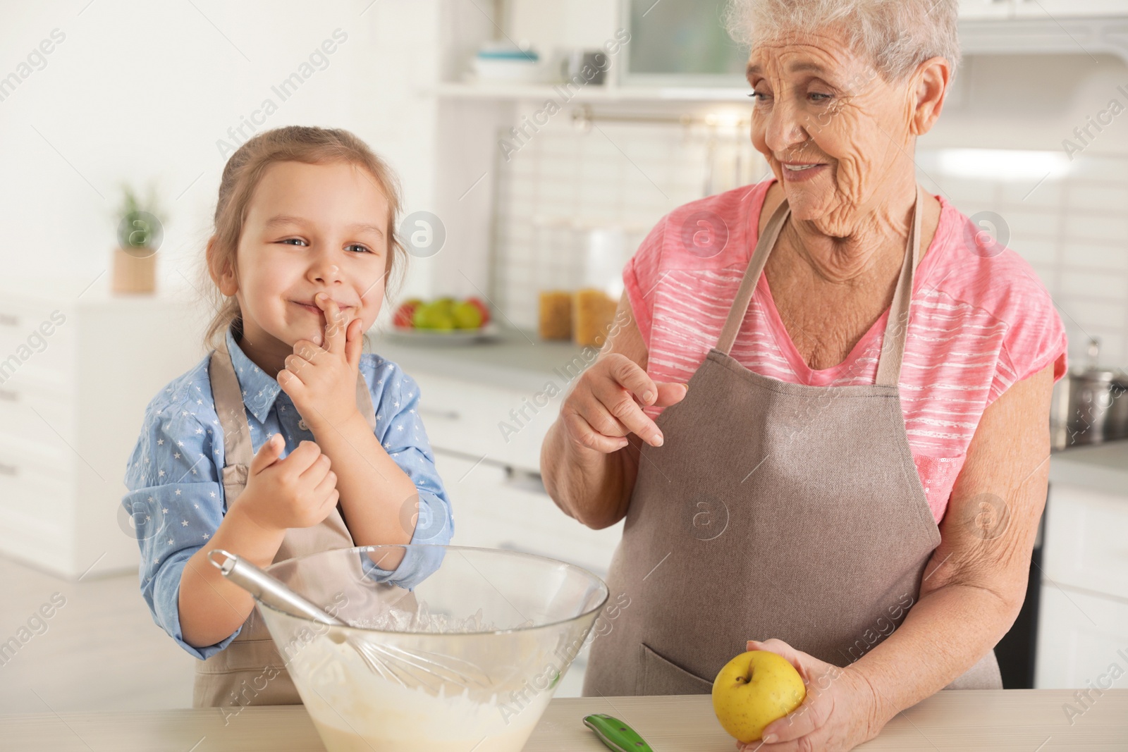 Photo of Cute girl and her grandmother cooking in kitchen