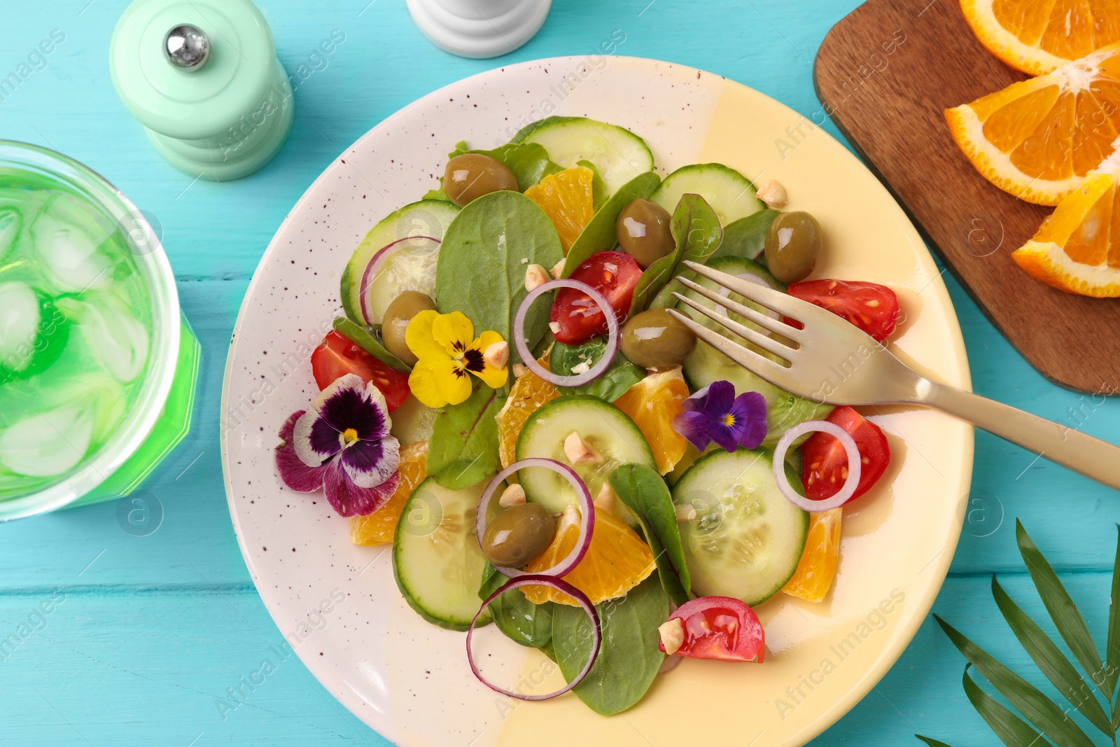 Photo of Delicious salad with orange, spinach, olives and vegetables served on turquoise wooden table, flat lay