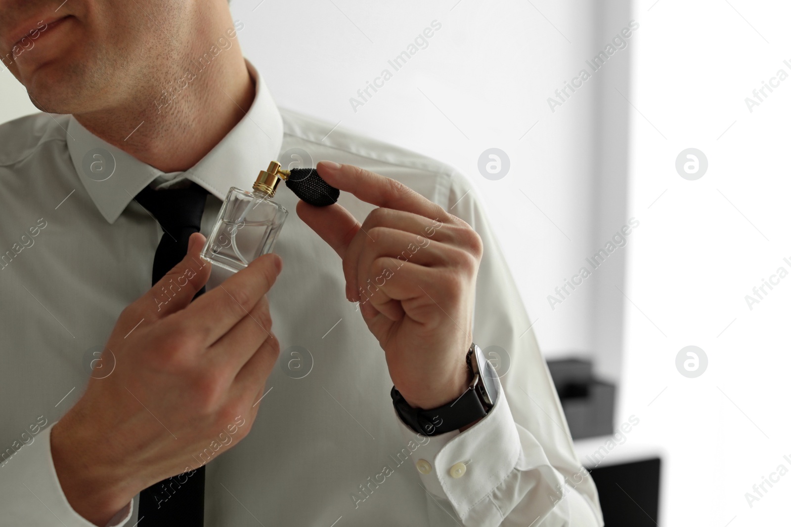 Photo of Handsome man applying perfume on neck indoors, closeup. Space for text