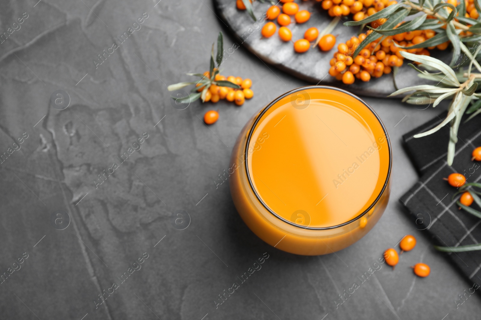 Photo of Sea buckthorn juice and fresh berries on black table, flat lay. Space for text