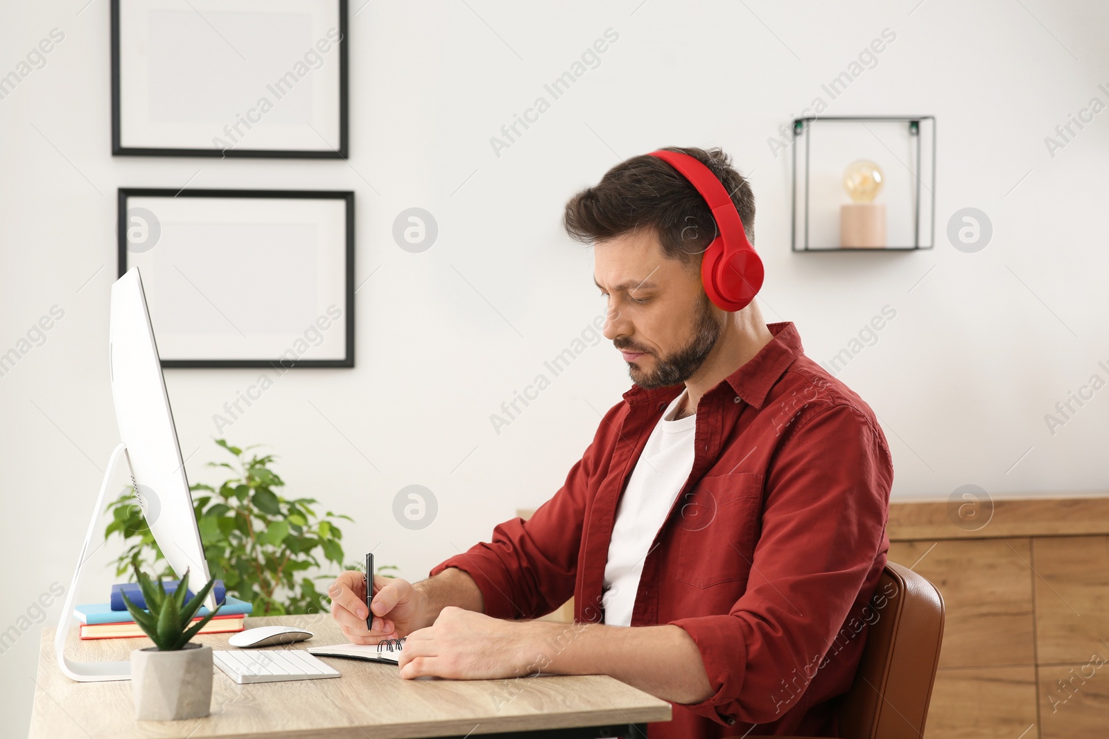 Photo of Online translation course. Man in headphones writing near computer at home