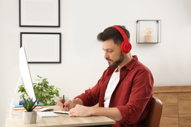 Photo of Online translation course. Man in headphones writing near computer at home