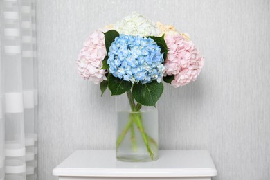 Photo of Beautiful hydrangea flowers in vase on white bedside table indoors