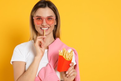 Young woman eating French fries on yellow background, space for text