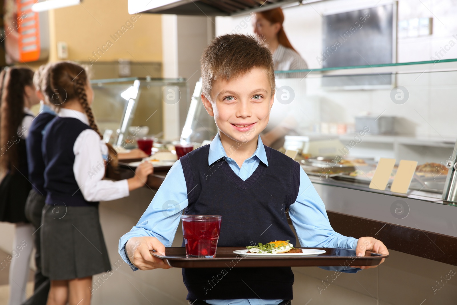 Photo of Cute boy holding tray with healthy food in school canteen