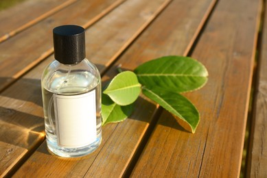 Photo of Bottle of perfume and green leaves on wooden table, space for text