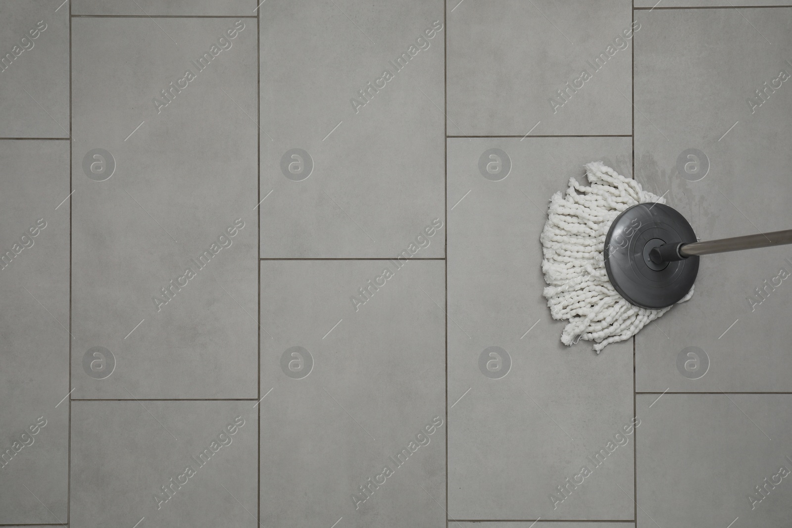 Photo of Cleaning grey tiled floor with string mop, top view. Space for text