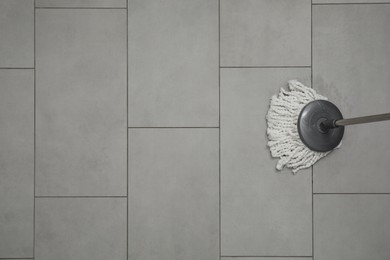 Cleaning grey tiled floor with string mop, top view. Space for text