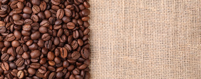 Photo of Many coffee beans on burlap fabric, top view. Space for text