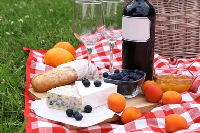 Photo of Picnic blanket with delicious food and wine outdoors on summer day, closeup