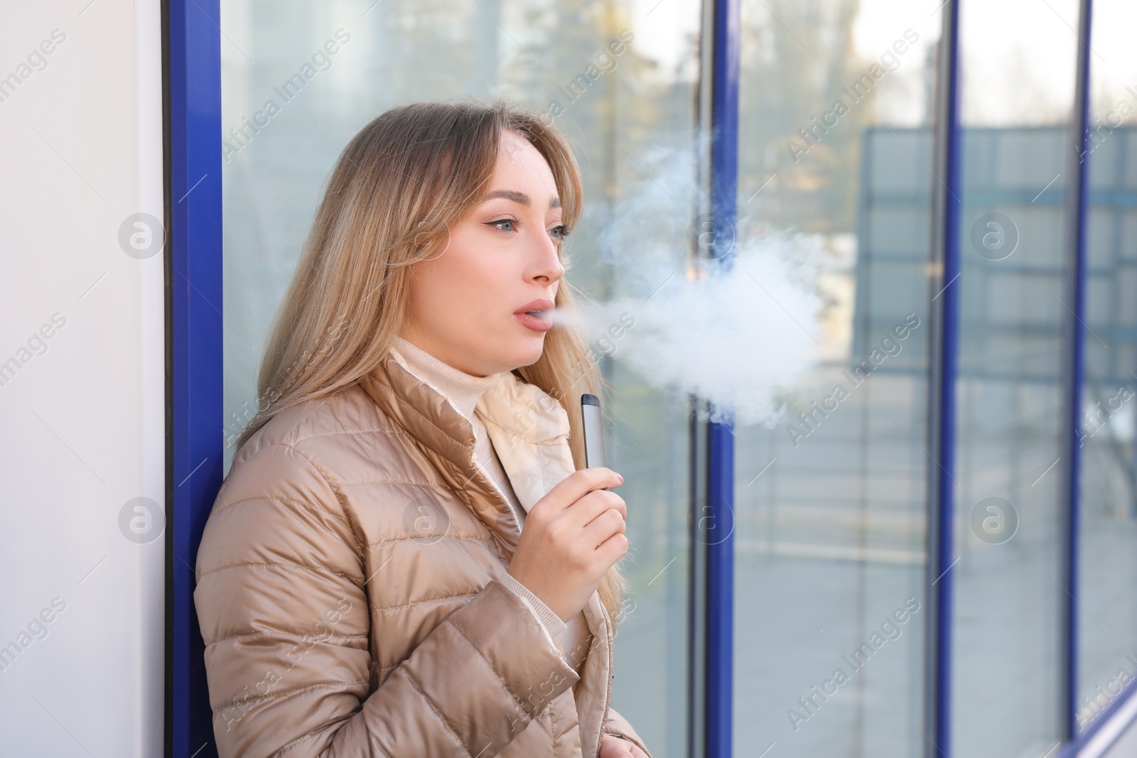 Photo of Beautiful young woman using disposable electronic cigarette outdoors