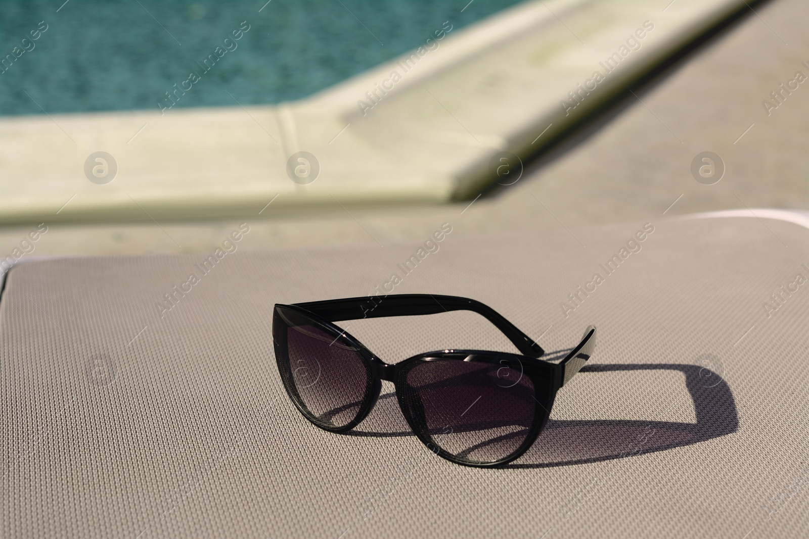 Photo of Stylish sunglasses near outdoor swimming pool on sunny day, space for text