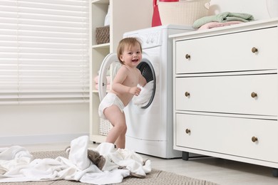 Happy girl pulling baby clothes out of washing machine indoors