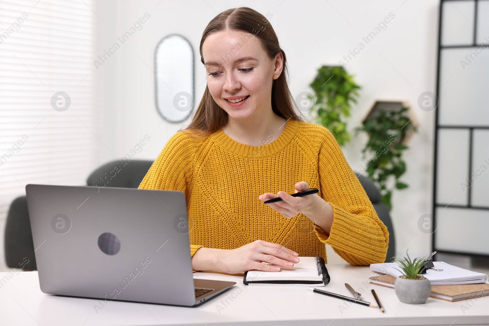 Photo of E-learning. Young woman using laptop during online lesson at white table indoors