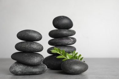 Photo of Stacks of spa stones and green leaves on grey table, space for text