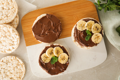 Photo of Puffed rice cakes with chocolate spread, banana and mint on grey marble table, flat lay