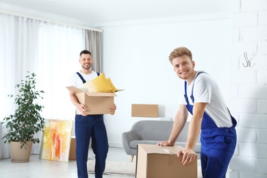 Moving service employees with cardboard boxes in room