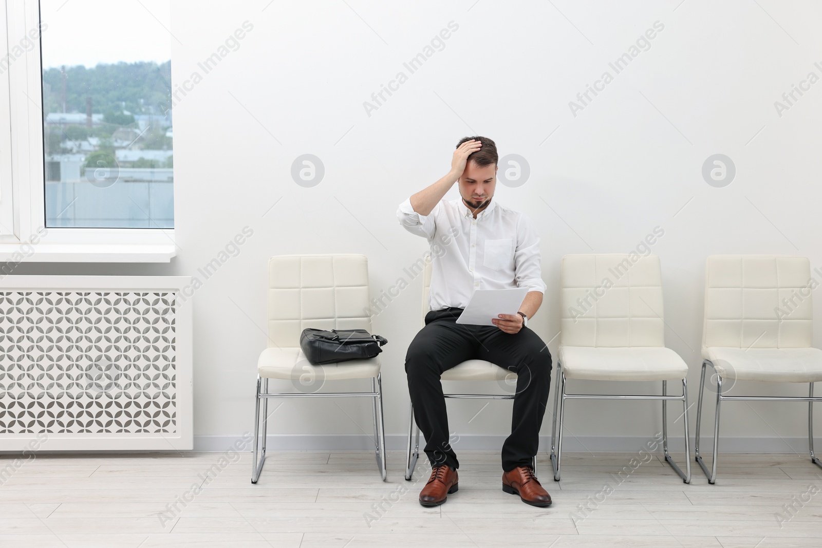 Photo of Man with sheet of paper waiting for job interview indoors