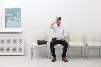 Photo of Man with sheet of paper waiting for job interview indoors