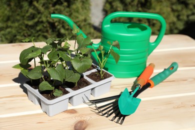 Photo of Seedlings growing in plastic containers with soil, gardening tools and watering can on wooden table outdoors