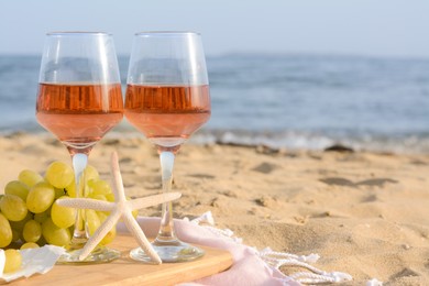 Photo of Glasses with rose wine and snacks on sandy seashore. Space for text