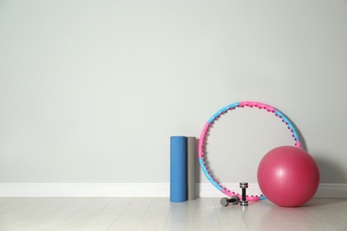 Photo of Hula hoop, exercise ball, yoga mat and dumbbells near light wall in gym. Space for text