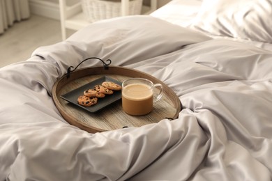 Photo of Delicious cookies and cup of coffee on bed with stylish silky linens indoors