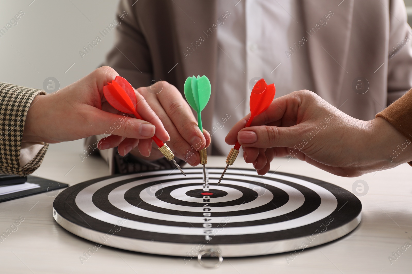 Photo of Business targeting concept. People with darts aiming at dartboard at table, closeup