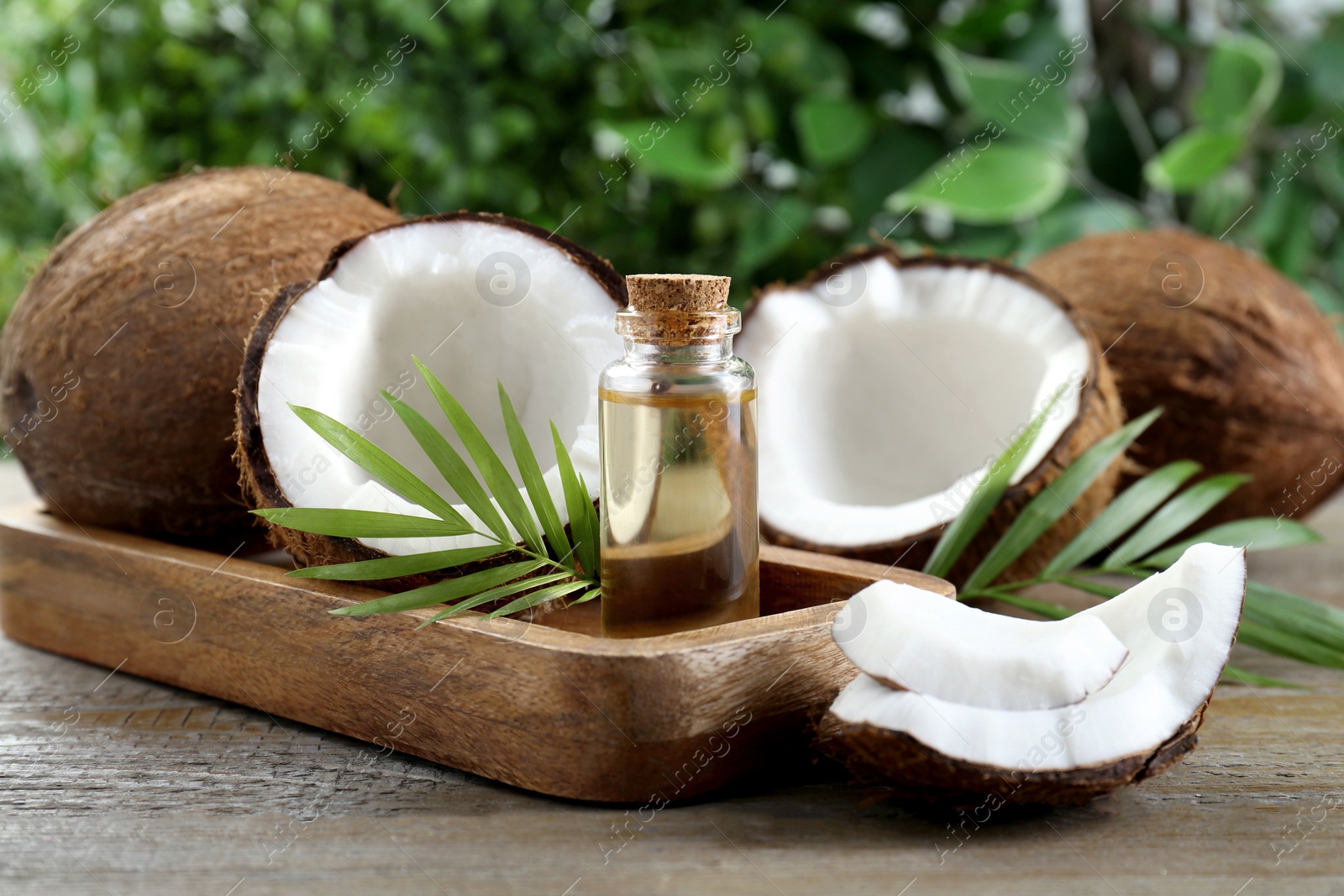 Photo of Bottle of organic coconut cooking oil, fresh fruits and leaves on wooden table