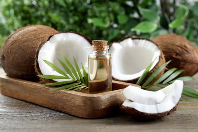 Photo of Bottle of organic coconut cooking oil, fresh fruits and leaves on wooden table