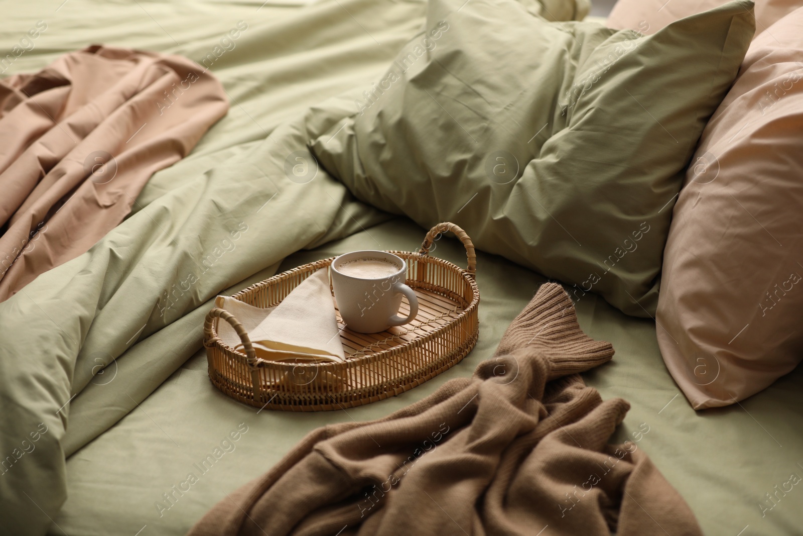 Photo of Cup of hot coffee on bed with pistachio linen in room