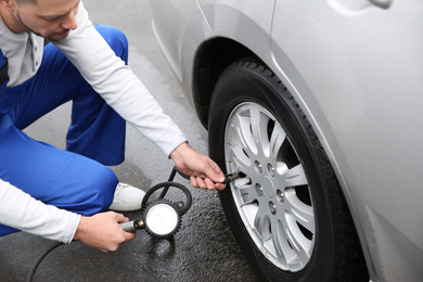 Mechanic checking tire pressure in car wheel at service station, closeup