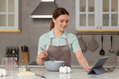 Woman with tablet computer cooking at table in kitchen