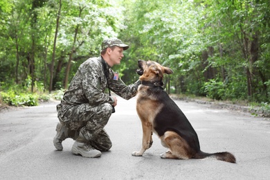 Photo of Man in military uniform with German shepherd dog, outdoors