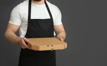 Waiter in apron with pizza box on grey background, space for text. Food delivery service