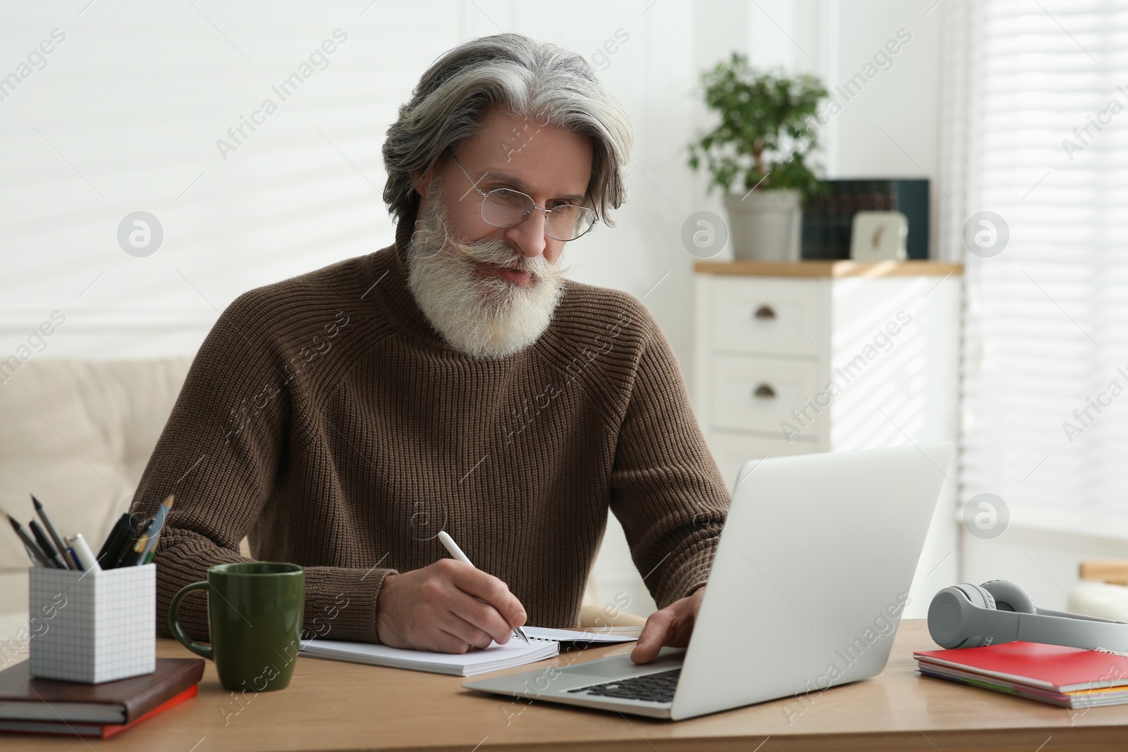 Photo of Middle aged man with laptop and notebook learning at table indoors