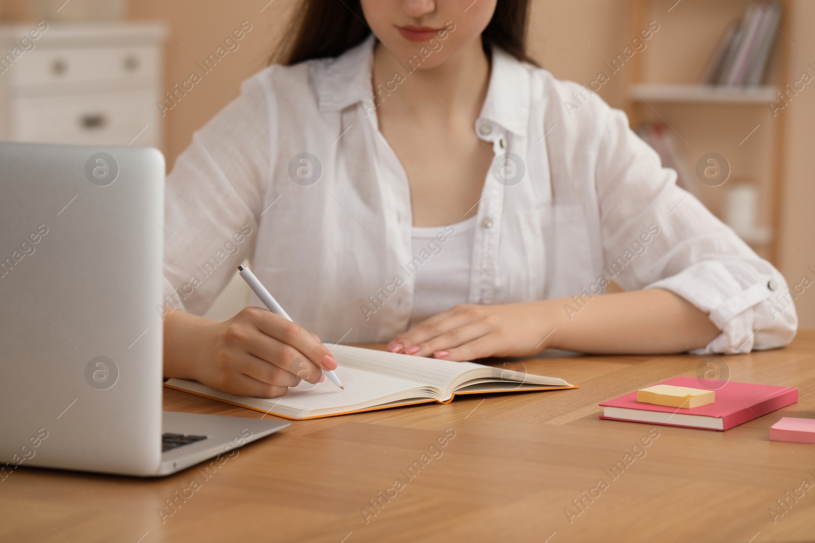 Photo of Woman writing in notebook at wooden table indoors, closeup