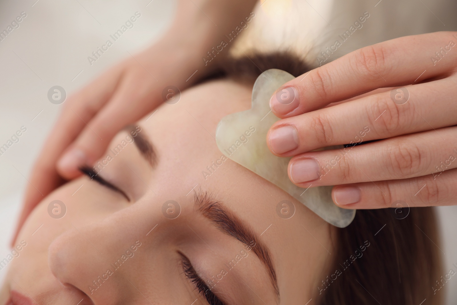 Photo of Young woman receiving facial massage with gua sha tool in beauty salon, closeup