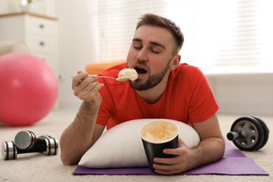 Photo of Lazy young man eating ice cream instead of training at home