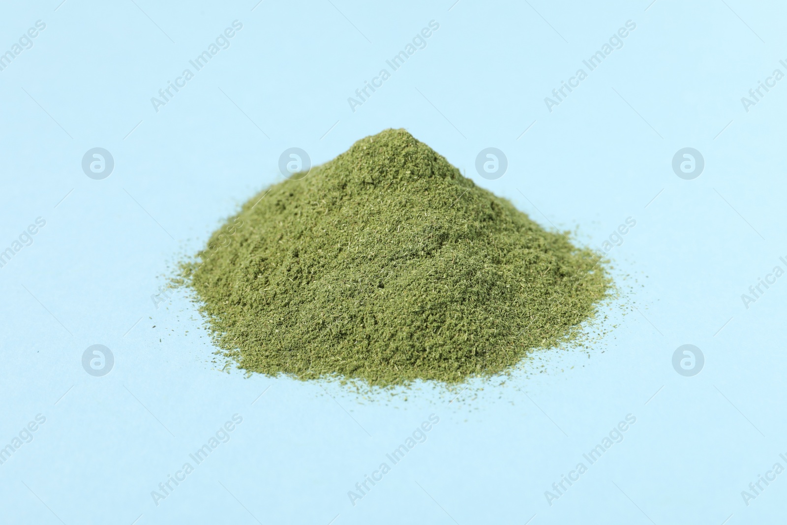 Photo of Pile of wheat grass powder on light blue table, closeup