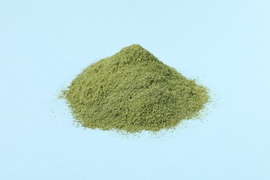 Pile of wheat grass powder on light blue table, closeup