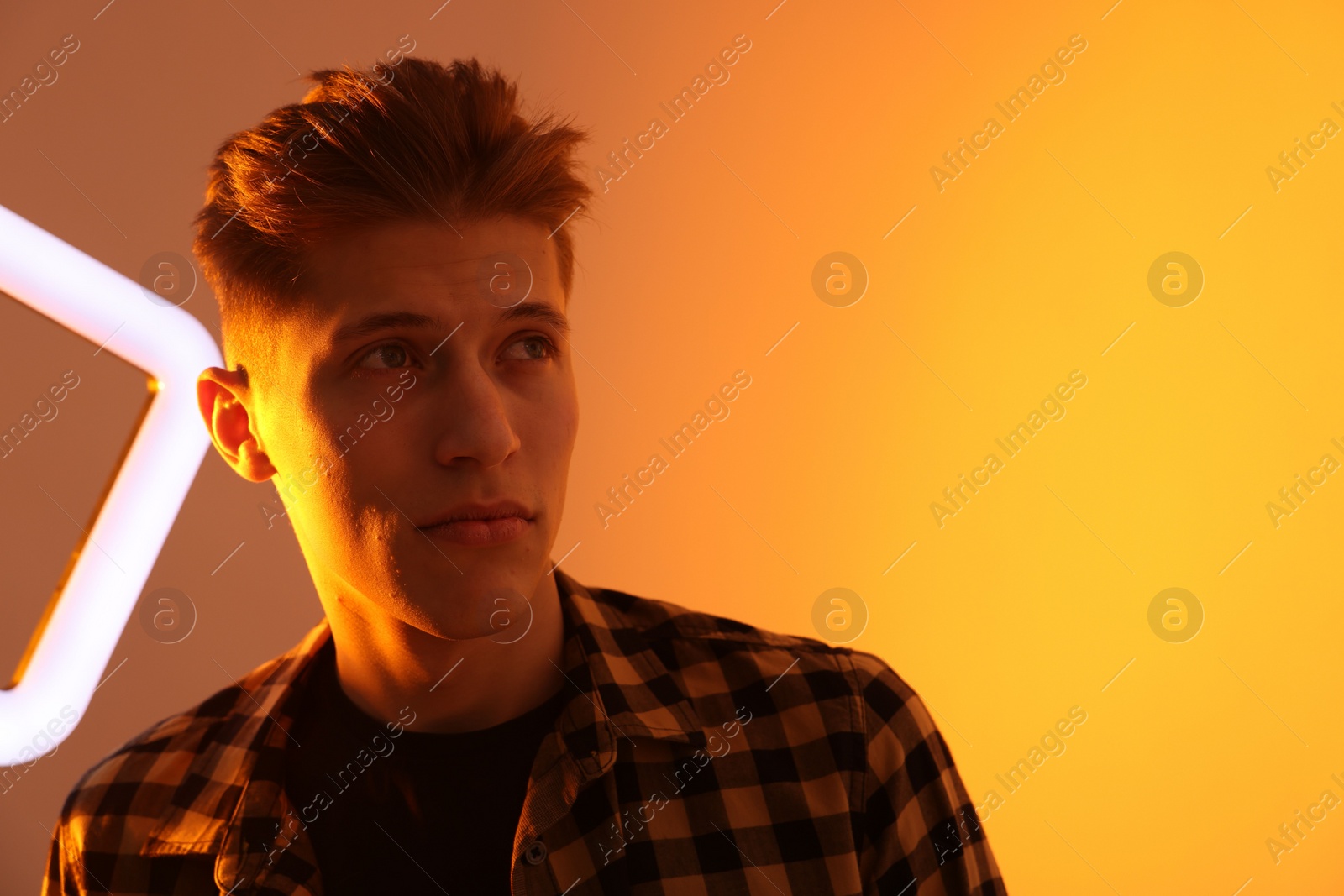 Photo of Young man with square lamp on color background in neon lights. Space for text