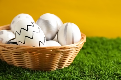 Photo of Wicker basket of painted Easter eggs on green lawn against color background, closeup