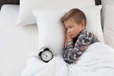 Photo of Cute boy with alarm clock sleeping in bed, above view
